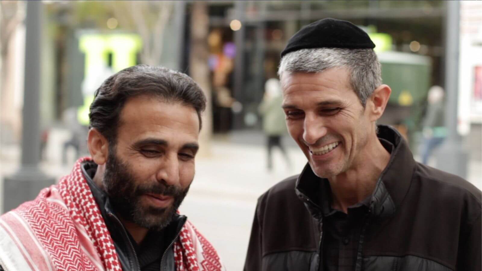 Muslim man and Jewish man standing next to each other on the street talking and smiling