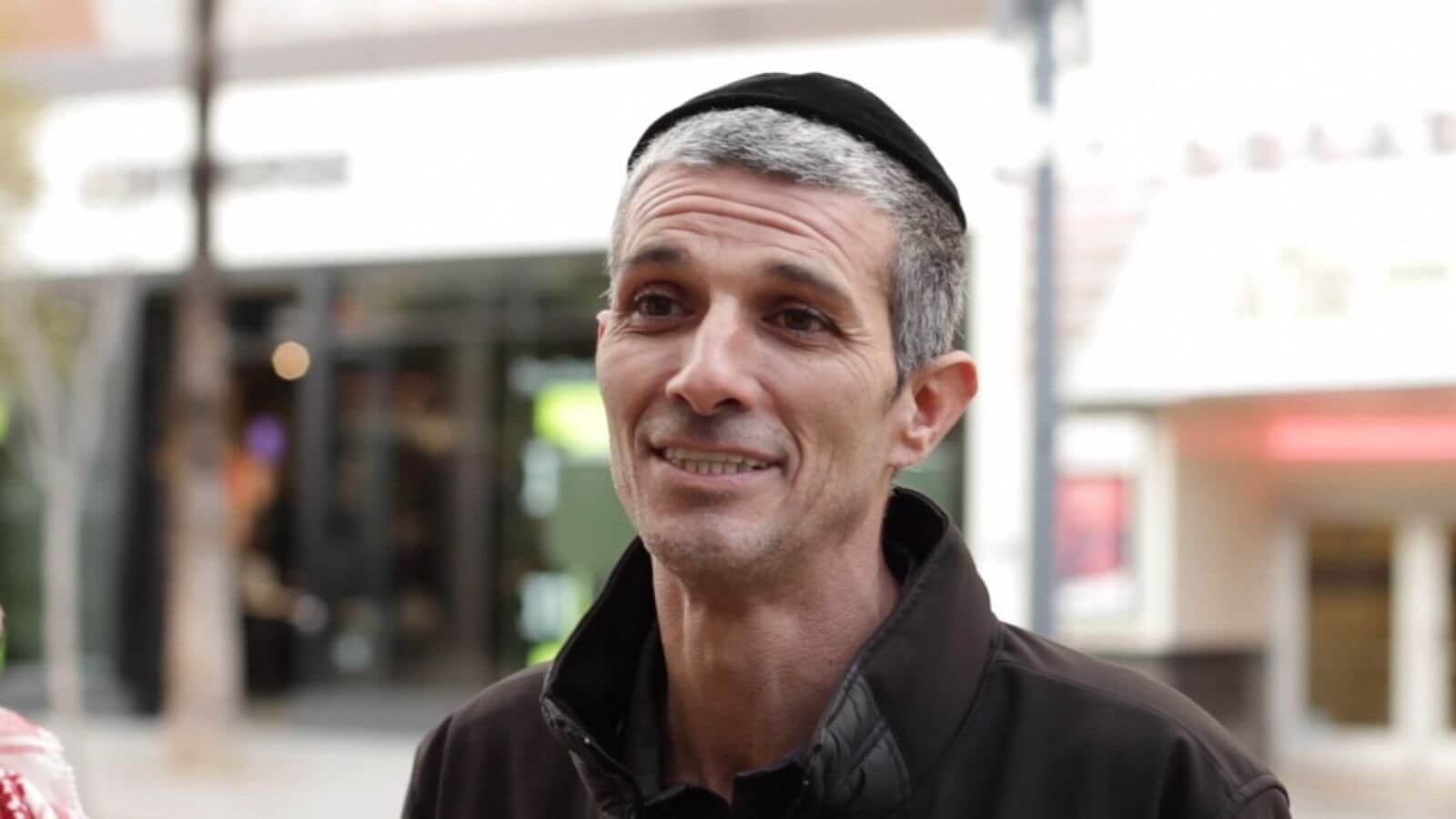 Older, thin Jewish man standing on the street talking and smiling