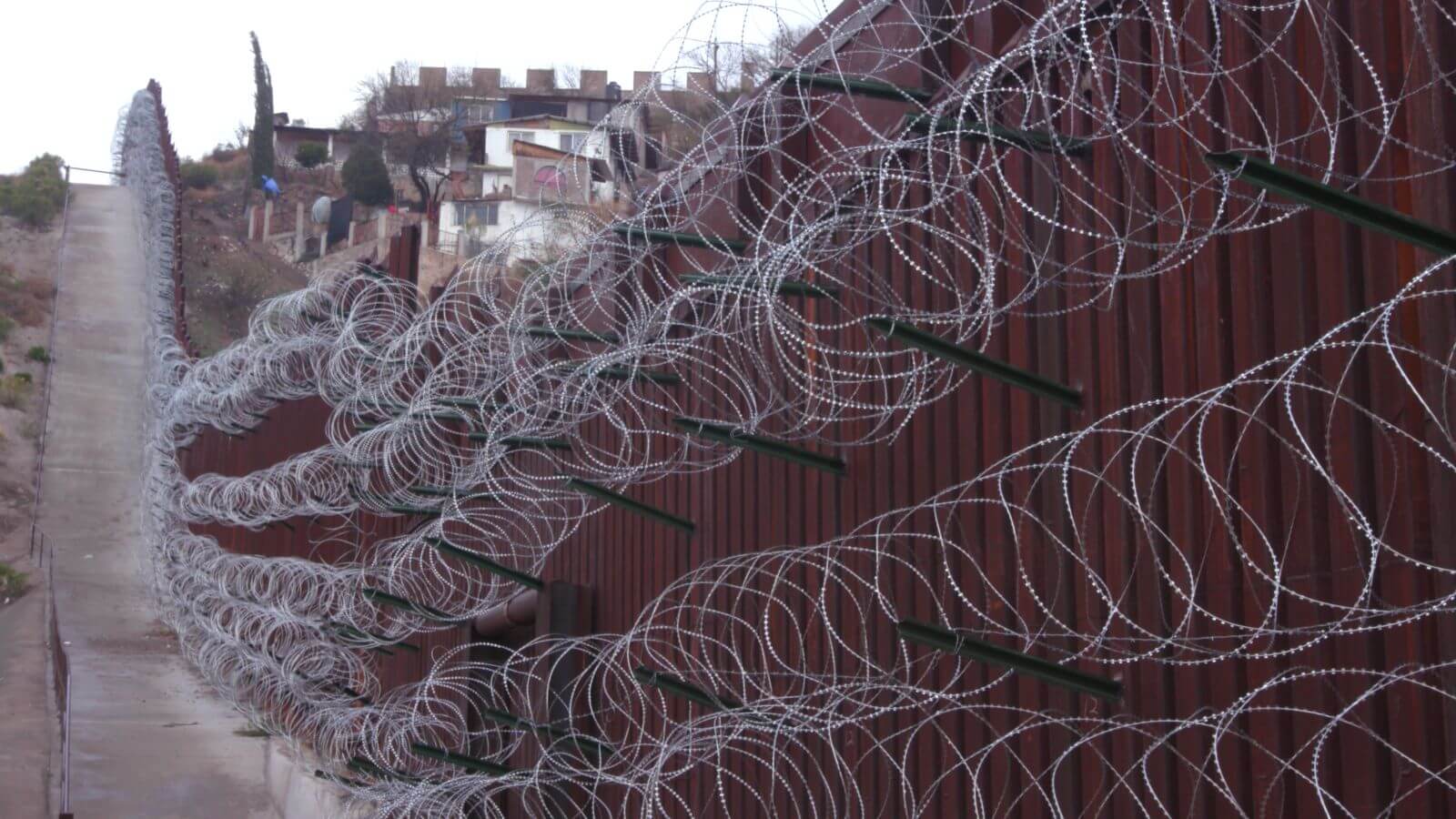 Brown border fence with long, running loops of barbed wire