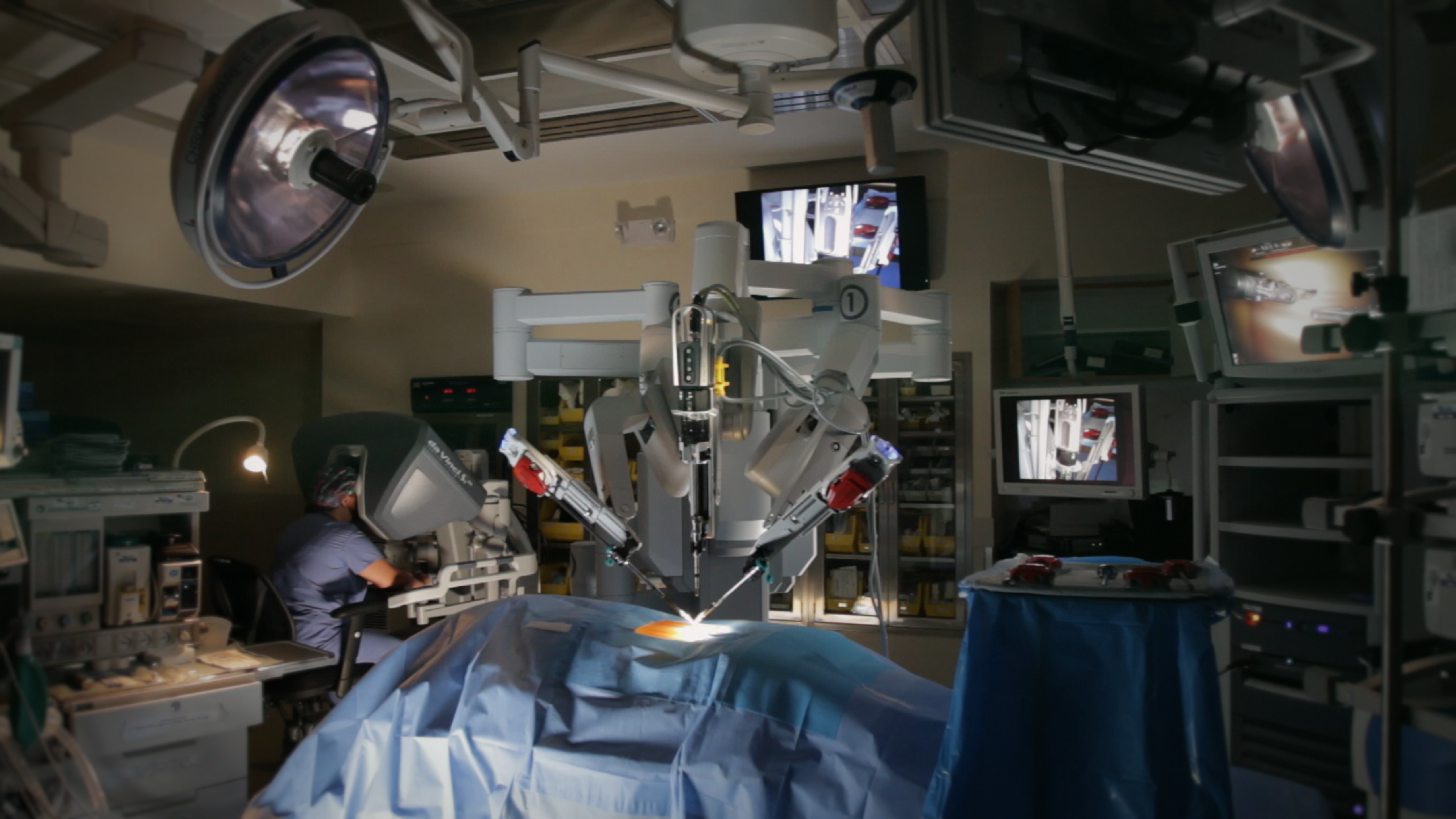 An operating room where a doctor is using a computer and robotic arms to perform a surgery