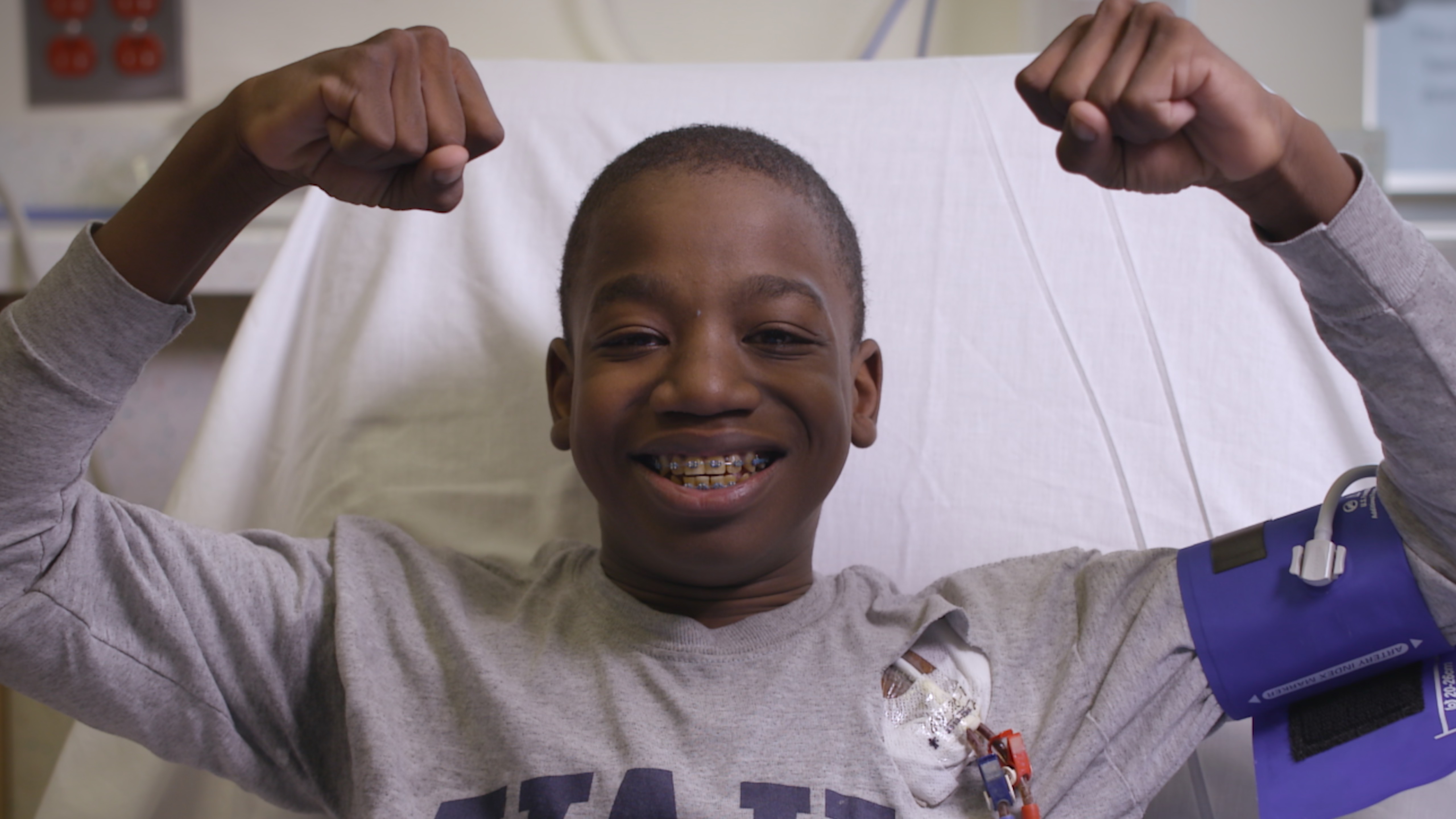 Boy in hospital bed smiling and holding up his arms in a strong muscles pose