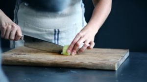Close up image of chef cutting an onion on a wooden cutting board