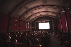 Large, old movie theatre with red seats, an arched ceiling and people seated throughout