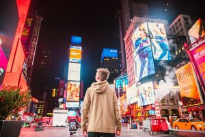 Man standing in Times Square looking up at advertisements on the buildings at night