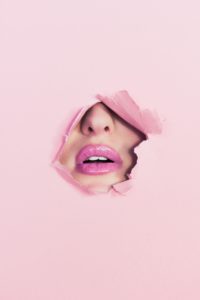 A woman's mouth and nose peeking through a torn pink heavy paper screen