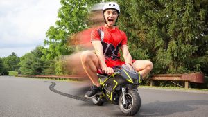 Teen boy in red shirt and shorts riding a micro motorbike down the road