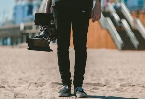 Lower half of man wearing black pants and holding a video camera