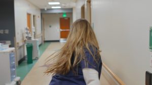 Woman in blue scrubs rushing down a hospital hallway