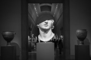 Black and white photo of ancient face sculpture and vases in an art museum